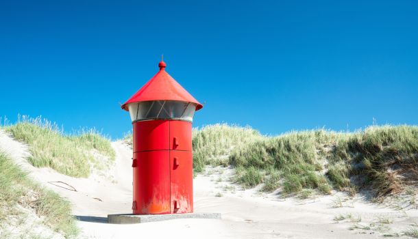 Ein roter Leuchtturm auf einer Sanddüne.