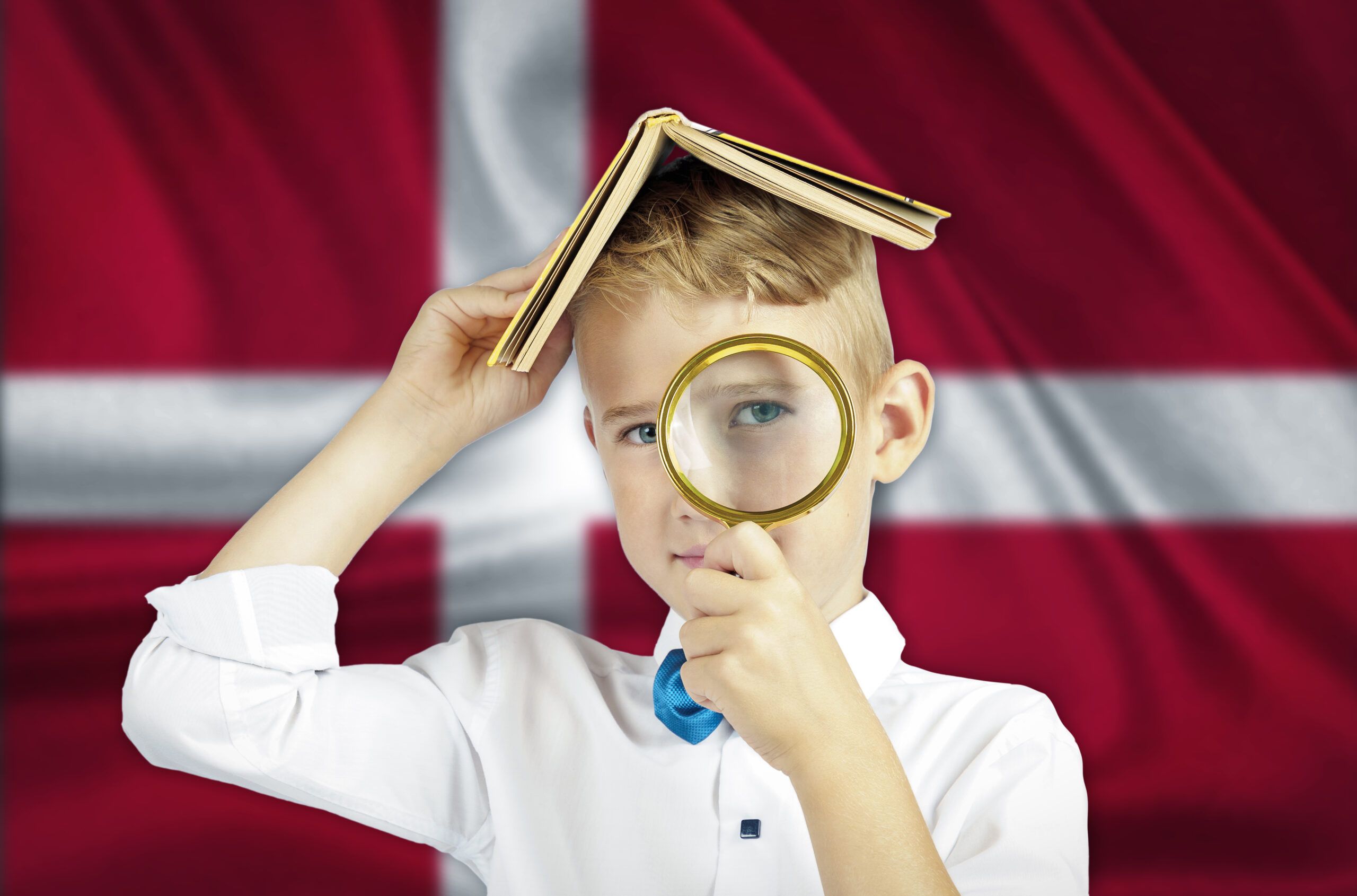 Ein Junge schaut durch eine Lupe vor einer dänischen Flagge.