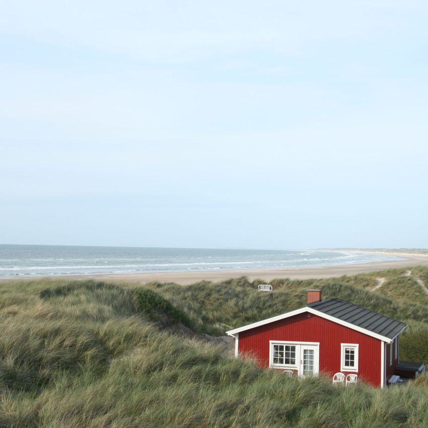 Ein kleines rotes Haus steht auf einem grasbewachsenen Hügel am Meer.