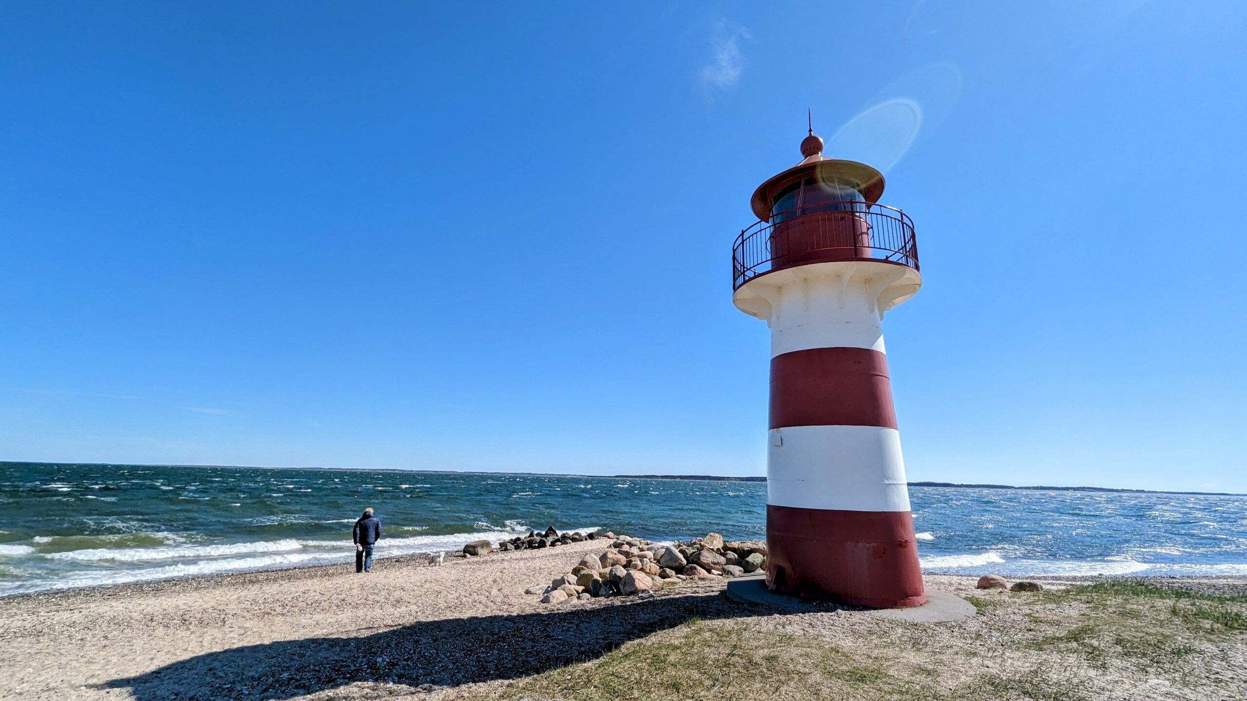 Ein Leuchtturm am Strand mit einer Person, die daneben steht.